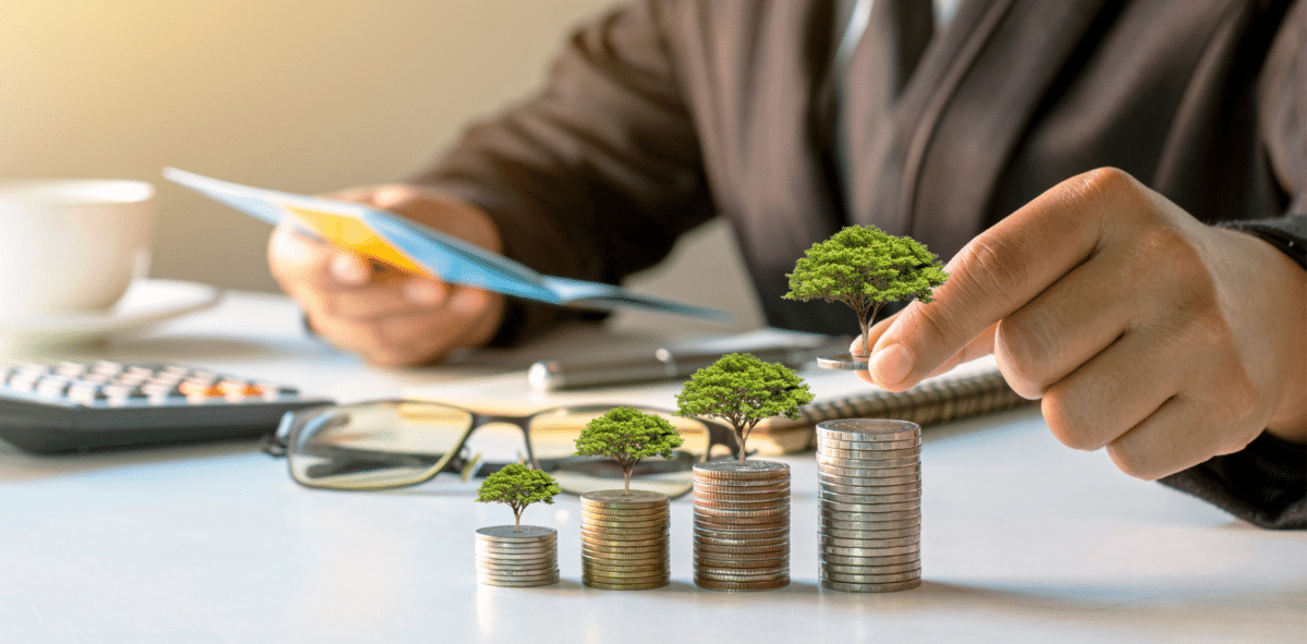 Businessman putting money on stack of coins with tree on top of it